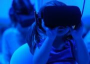 The photo displays a blue image with a child wearing a VR headset and using both hands to keep it in place.