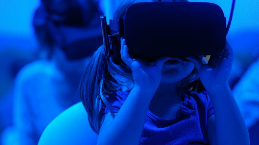 The photo displays a blue image with a child wearing a VR headset and using both hands to keep it in place.